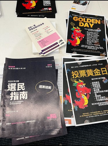 A table of voter guides, palm cards and an illustrated flyer with a dragon promoting Golden Day, in Chinese.